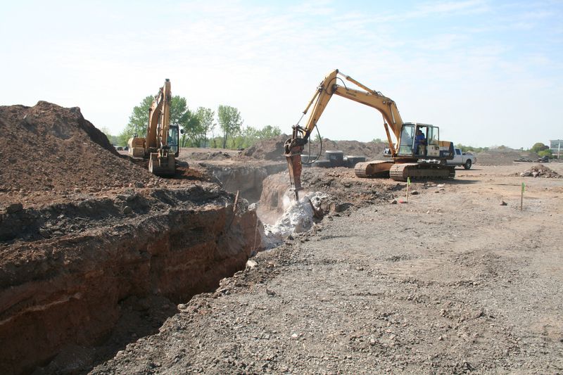 Two excavators removing concrete along a trench
