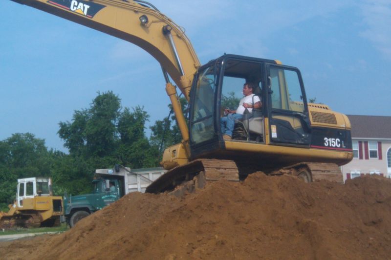 Excavator on a soil pile with a loader and dump truck behind