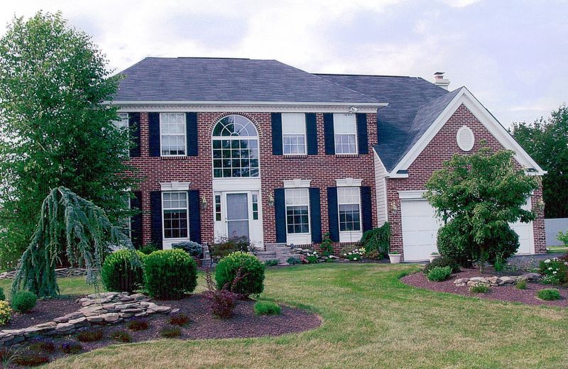 Two-story brick-front colonial with a Palladian window and landscaped beds